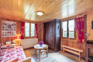 Une pièce de cabane en bois comprenant un lit, une table avec un vase, un banc et une grande porte en bois.