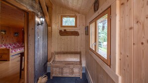 L’intérieur d’une cabane en bois, avec un banc, une fenêtre et une porte donnant sur une autre pièce.