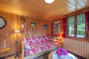A wooden cabin interior with a sofa, a clock, a lamp, and a window with curtains.