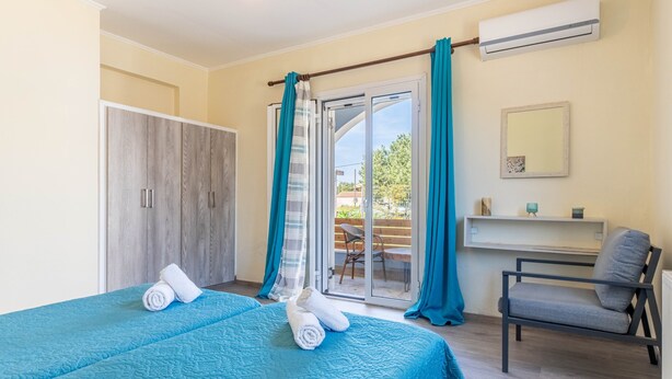 A bedroom with a bed, a chair, a desk, a wardrobe, and a sliding glass door to an outdoor area.