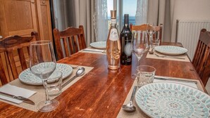 Une table à manger dressée avec des assiettes, des verres et des bouteilles, et une vue sur la mer par la fenêtre.