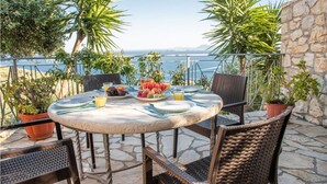Une table ronde entourée de chaises, une assiette de fruits et des boissons, le tout disposé sur une terrasse au sol en pierre et agrémentée de plantes en pot.