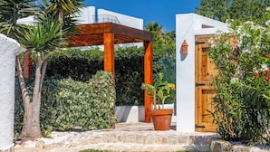 Une cour avec une pergola en bois, un pot de fleurs et une porte dotée d’une poignée décorative.