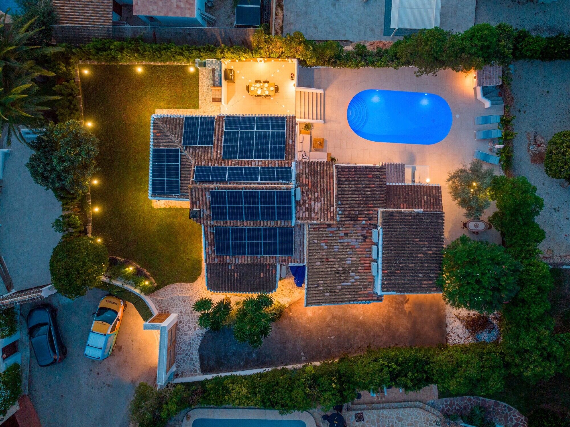 An aerial view of a residential property with a swimming pool, solar panels, and a patio area.
