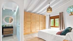 Une chambre à coucher comprenant un lit, une armoire en bois, un miroir rond, une fenêtre avec des rideaux et un luminaire suspendu.