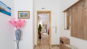 Un pasillo con un espejo, un florero con flores rosadas y una puerta que da a otra habitación.