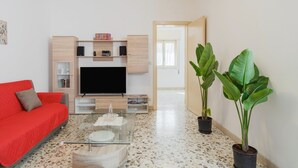 Una sala de estar moderna con un sofá rojo, un televisor de pantalla plana, una mesa de centro y dos plantas en macetas.