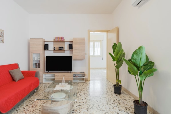 Una sala de estar moderna con un sofá rojo, un televisor de pantalla plana, una mesa de centro y dos plantas en macetas.