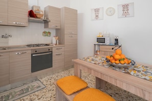 Una cocina moderna con estufa a gas, horno y microondas, una mesa de comedor con fruteros, y un estante con utensilios de cocina.