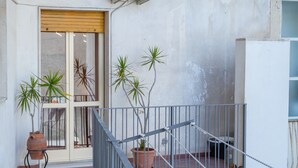 Un balcón con macetas, una puerta de madera y una baranda metálica.