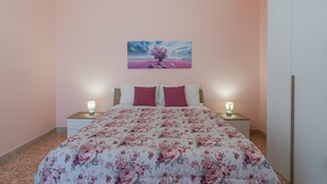Un dormitorio con una colcha estampada de flores, dos lámparas de noche, una mesita de noche y un cuadro colgado en la pared.