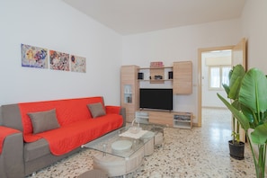 Una sala de estar moderna con un sofá rojo, una mesa de centro de cristal, un televisor de pantalla plana, armarios de madera y obras de arte en la pared.
