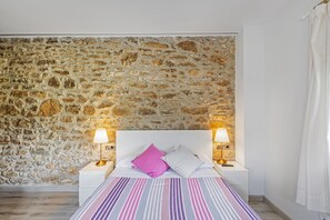 A bedroom with a stone wall, a bed with striped bedding, two bedside lamps, and a white headboard.