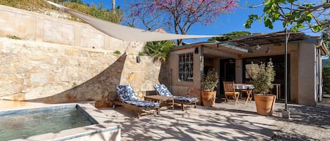 Zona junto a la piscina con sillones, una piscina pequeña y un patio con mesa y sillas.
