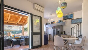 A modern kitchen with a dining area, featuring a large refrigerator, a dining table with chairs, and a view through a glass door to an outdoor patio.