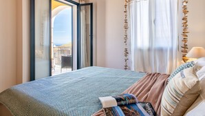 A bedroom with a bed, a window with curtains, and a view of buildings outside.