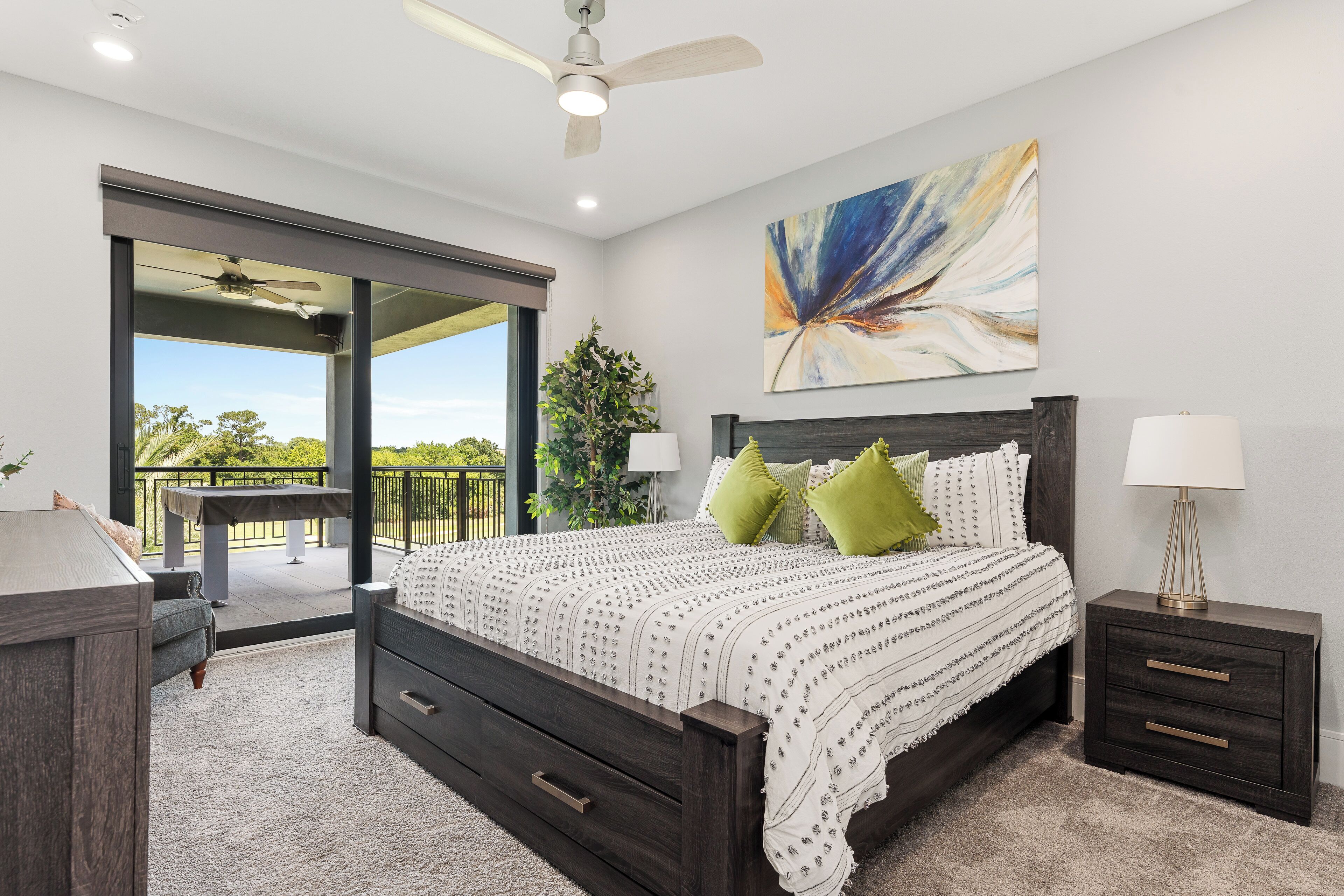 A bedroom with a large bed, a nightstand, a desk, and a view of the outdoors.