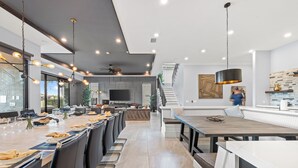 Une cuisine moderne dotée d’un grand îlot central, d’appareils électroménagers intégrés et d’un coin repas avec un plafond haut et des luminaires suspendus.