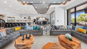Un salon moderne avec un canapé d’angle, des tables basses en bois et un coin repas avec une cuisine en arrière-plan.