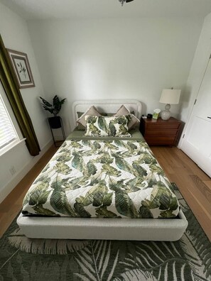 A bed with a leaf-patterned bedspread, a bedside table with a lamp, and a potted plant. - Osage Oasis: Pool, Hot Tub, Near Downtown & Trails (Bentonville)