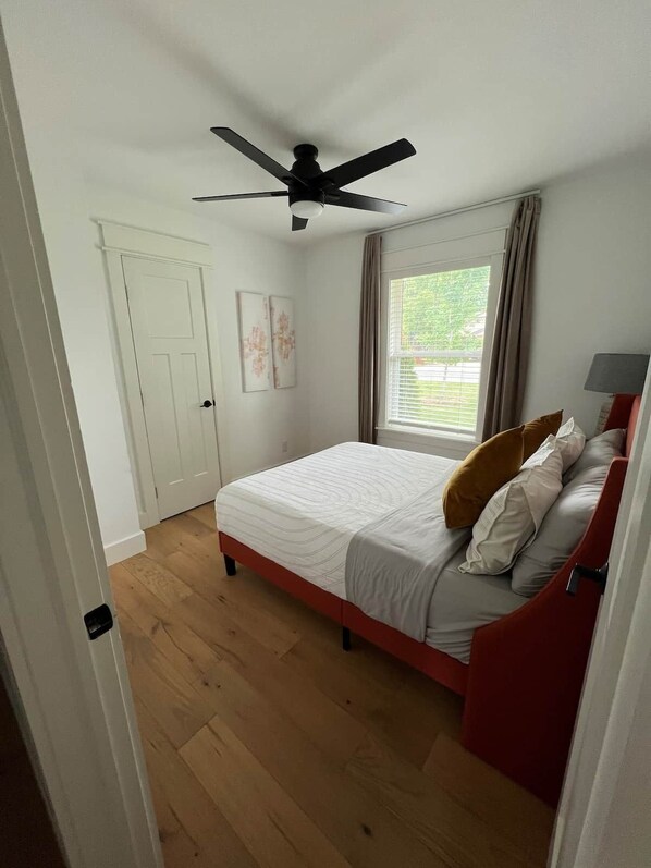 Un dormitorio con cama, ventilador de techo, ventana con cortinas y una puerta.