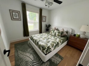 A bedroom with a bed, bedside table, lamp, and a window with curtains.