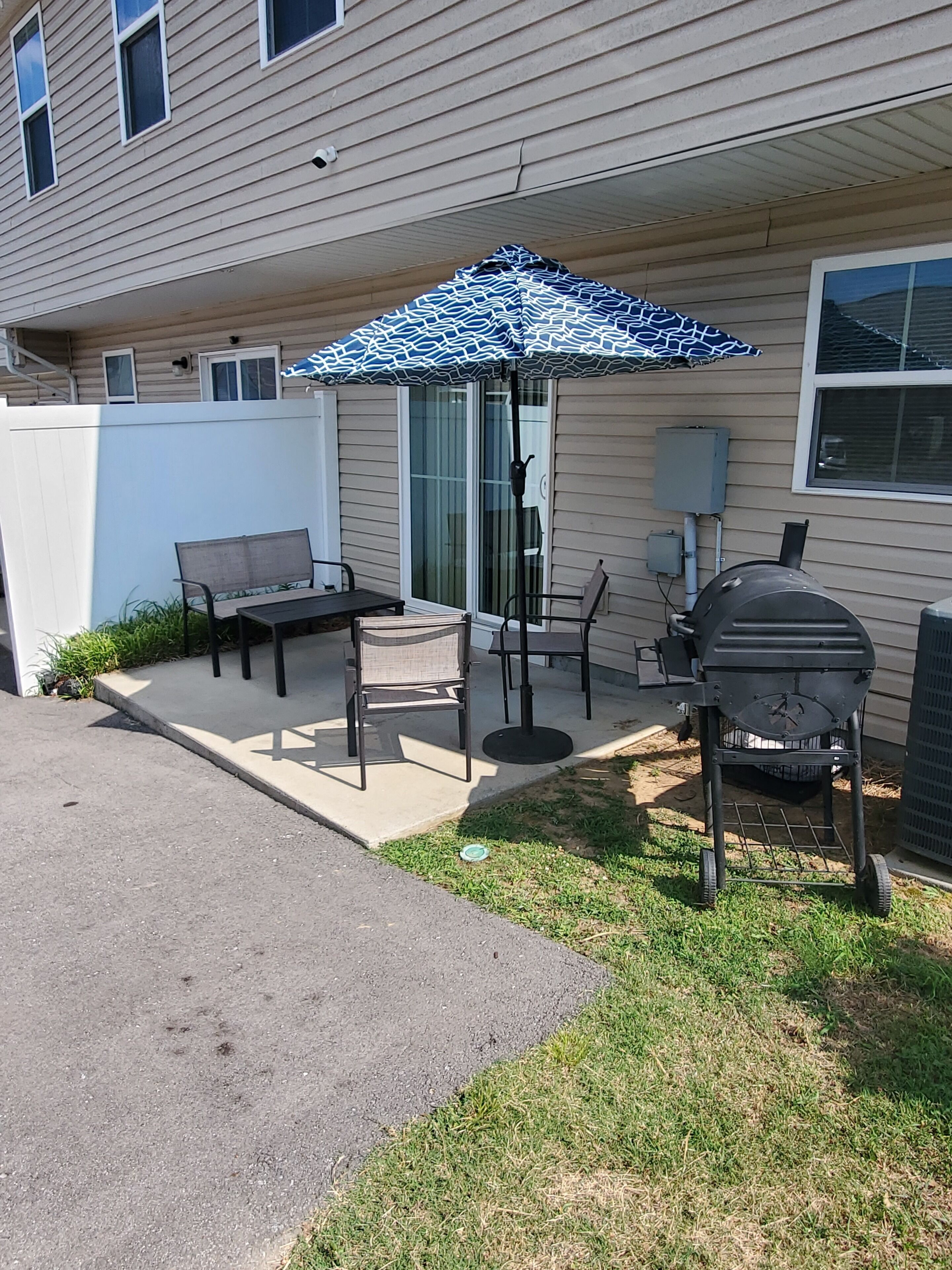 A patio with outdoor furniture, a grill, and a patterned umbrella.