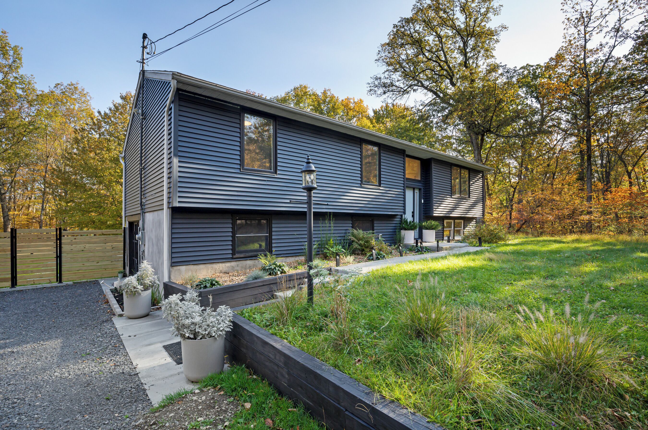 Une maison moderne à deux étages, dotée d’un toit en pente, d’un porche à l’avant et d’un jardin aménagé avec des plantes en pot et une terrasse en bois.
