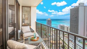 A balcony with a view of the ocean and cityscape, a table with a tray, and a chair.