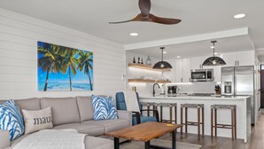 A modern living room with a sofa, coffee table, and a painting of a beach scene. - Fully Remodeled Ocean Front Comfort HKOK316 (Kihei)