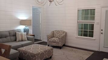 A living room with a sofa, armchair, ottoman, chandelier, and a door with a window.