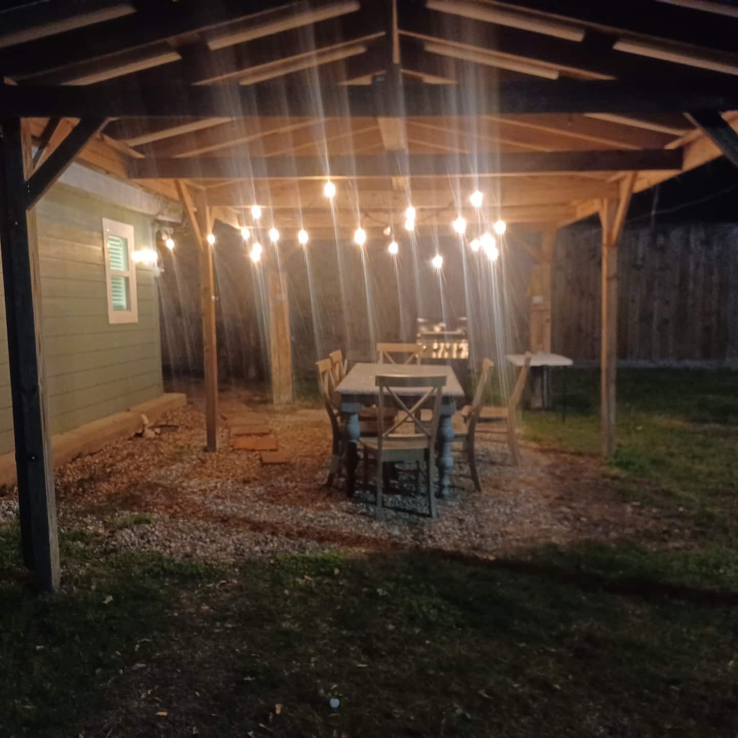An outdoor patio with a wooden pergola, string lights, a table, and chairs.