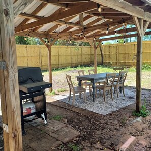 Um pátio externo com churrasqueira, mesa e cadeiras.
