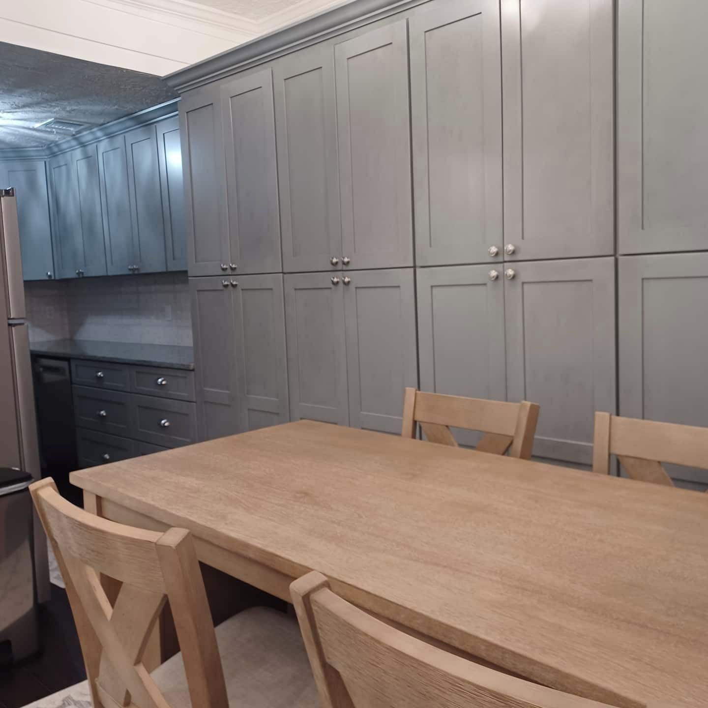 A kitchen with grey cabinets, a wooden table, and chairs.