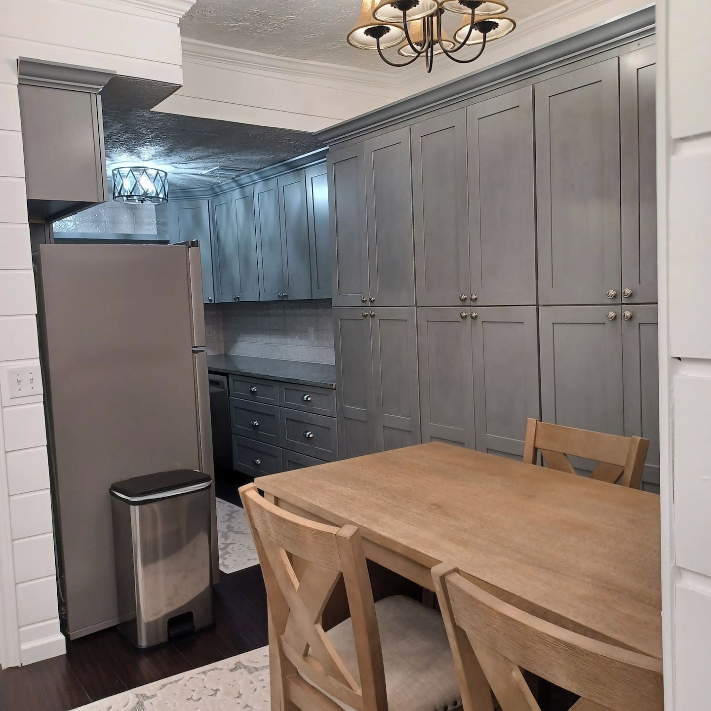 A kitchen with grey cabinets, a stainless steel refrigerator, and a wooden dining table with chairs.