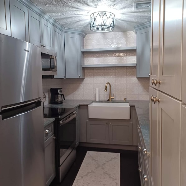 A compact kitchen with stainless steel appliances, a built-in oven, a coffee maker, and a sink with a gold faucet.