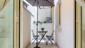 Eine schmale Außenpatio mit Tisch, Stühlen, einem großen Sonnenschirm und Topfpflanzen.