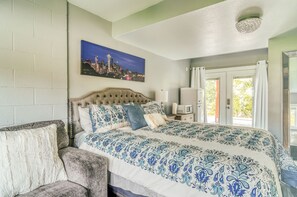 A bedroom with a bed, a chair, a painting of a cityscape, and a window with curtains.