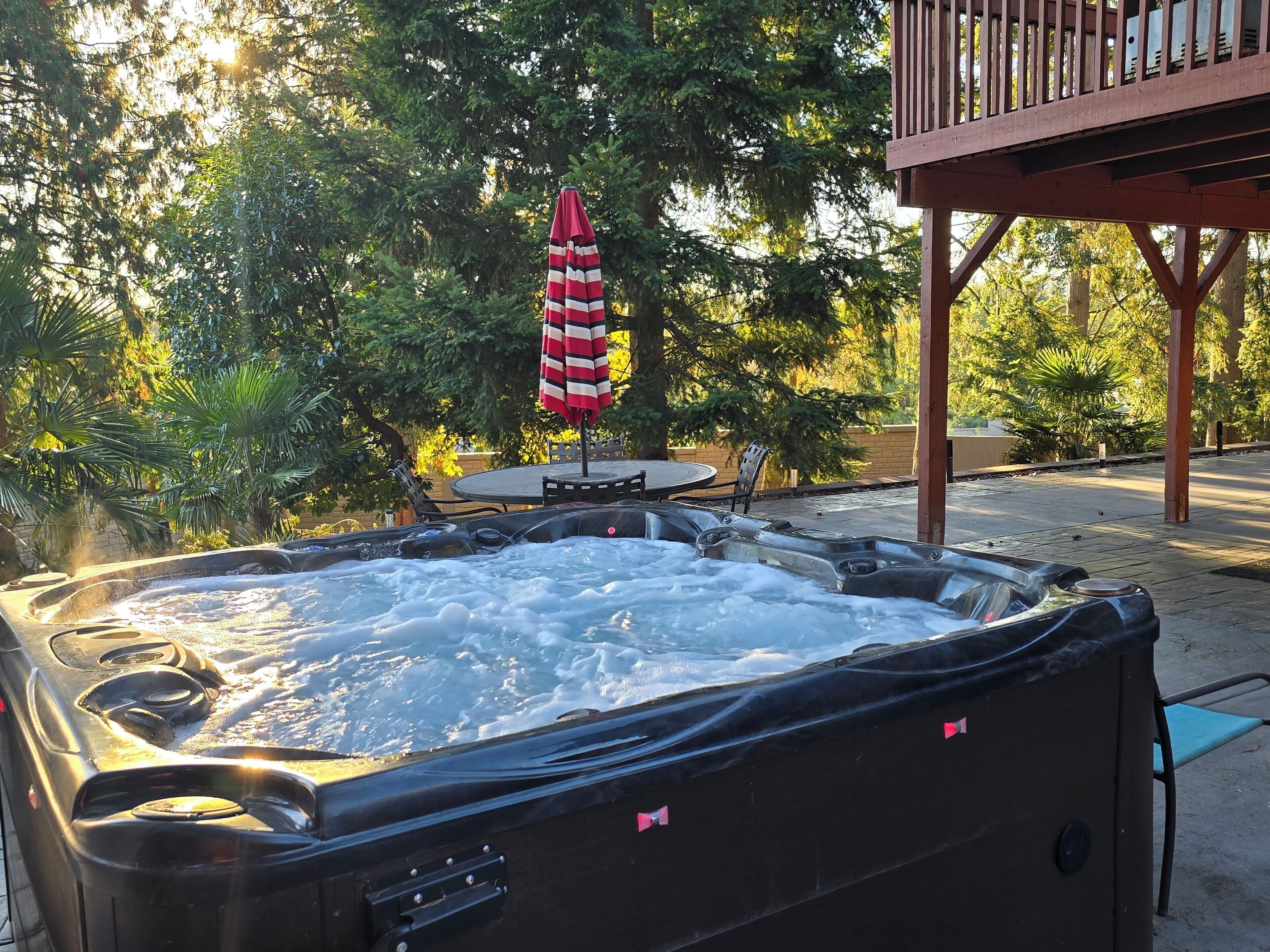 A hot tub with a table and chairs nearby, surrounded by trees.