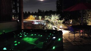 Una vasca idromassaggio con luci verdi, un patio con sedie e vista su un parcheggio sotto un cielo notturno con la luna visibile.