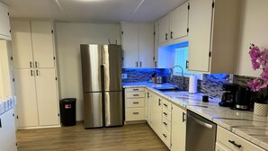 Une cuisine moderne avec des meubles blancs, un réfrigérateur en acier inoxydable, un pare-feu en carrelage et un plancher en bois.