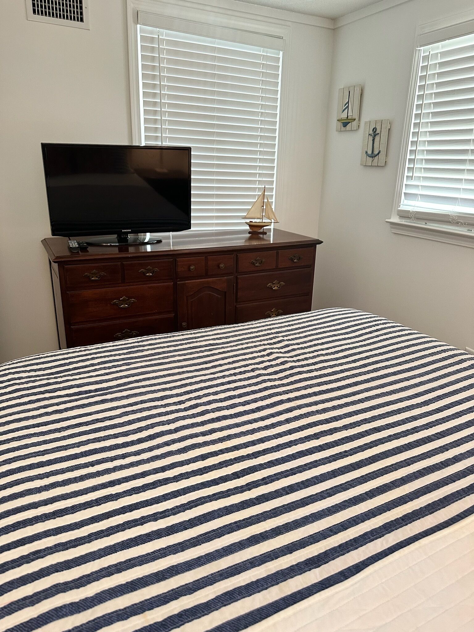 A bedroom with a bed, a dresser, a television, and two windows with blinds.