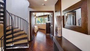 Un interior moderno con una escalera curva, un espejo grande y vistas de una habitación con cama y ventana.