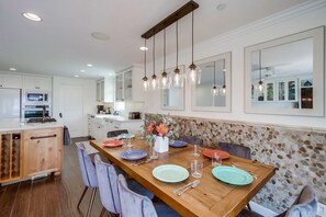 Een moderne keuken met witte kastjes, een houten eettafel gedekt met borden, en hangende hanglampen.