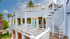 Een huis met twee verdiepingen, met een witte gevel, een overdekte patio met tuinmeubilair en een wenteltrap.