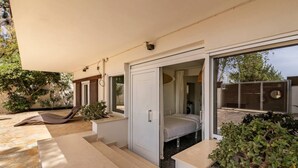 Un dormitorio moderno con cama, puerta corredera que da a un baño y balcón con una tumbona.