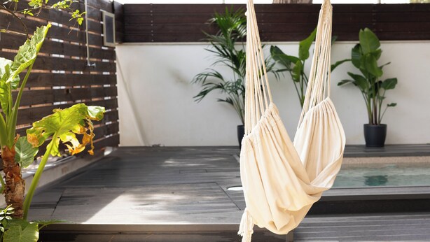 Una hamaca colgada de una viga de madera en un jardín con piscina y plantas en macetas.