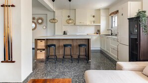 Una cocina moderna con una isla central, taburetes de bar y una zona de comedor con sofá.