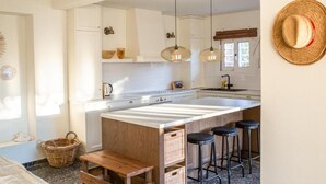 Una cocina moderna con una isla central, taburetes de bar, lámparas colgantes y un sombrero rústico en la pared.