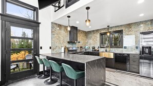 A modern kitchen with a large island, bar stools, and a view through a glass door. - Knife River Cabin with Amazing View and Sauna (Two Harbors)